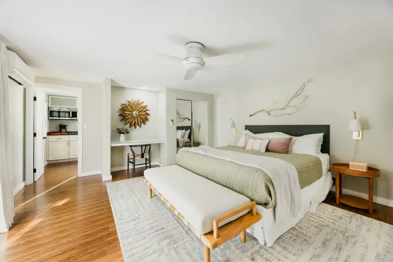 Cozy Palm Springs casita bedroom with warm wood floors, soft bedding, and sunburst mirror detail at Biskra House.