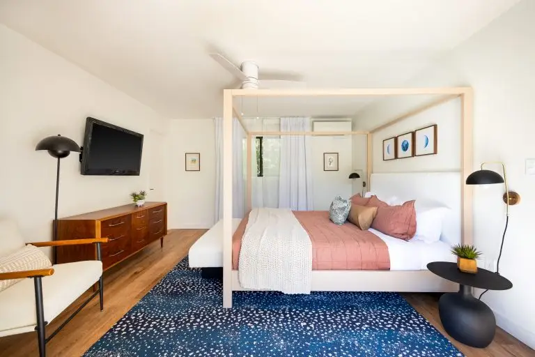 Modern en-suite bedroom with blush bedding, mid-century dresser, and black lighting accents at Biskra House vacation rental in Rancho Mirage, CA.