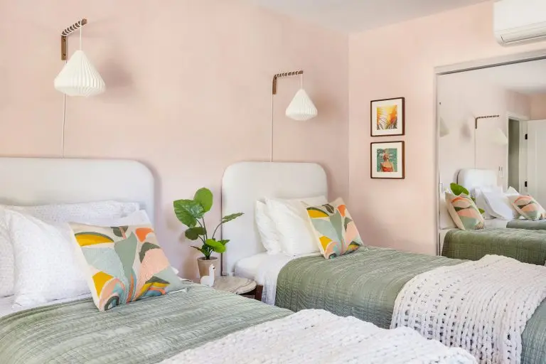 Cozy twin bedroom with blush walls, modern pendant lights, and soft green bedding at Biskra House vacation rental in Rancho Mirage, CA.