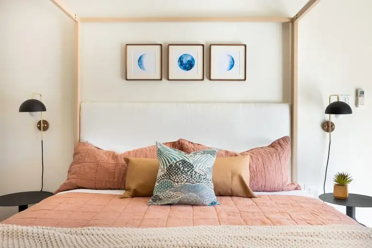 Cozy modern bedroom with framed moon artwork, wall sconces, and layered pillows in warm desert tones at Biskra House.