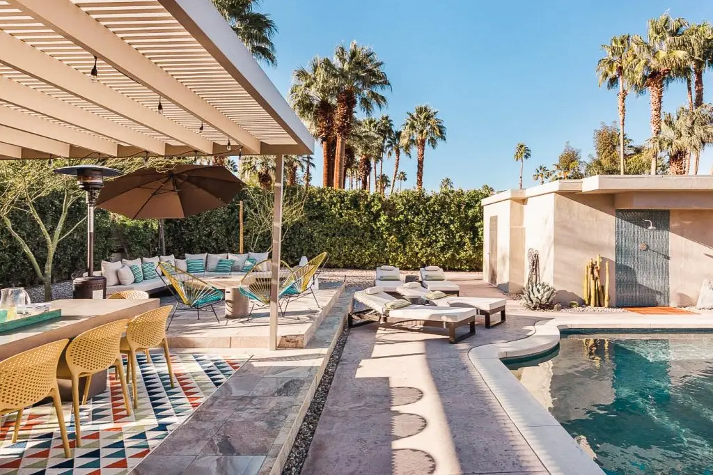 Modern Rancho Mirage vacation rental with pool, outdoor shower, lounge chairs, and covered dining area surrounded by palm trees at Biskra House.